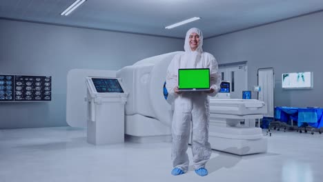 full body of asian male scientist smiling and showing green screen laptop while standing with mri machine in the hospital