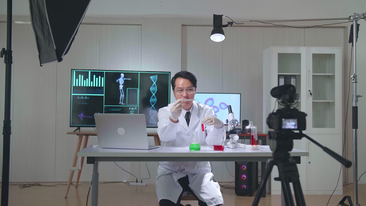 Young Asian Male Research Scientist Holding Glass Test Tube And Speaking To The Camera With Professional Lighting