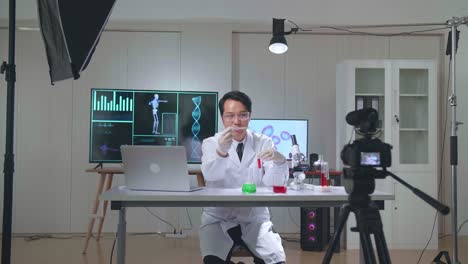 young asian male research scientist holding glass test tube and speaking to the camera with professional lighting