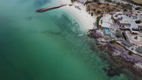 Playa-Caimancito-Y-La-Concha-En-La-Paz,-Baja-California,-Mostrando-Las-Aguas-Cristalinas-De-Color-Turquesa-Y-La-Playa-De-Arena-Blanca,-Con-Edificios-Costeros,-Vista-Aérea