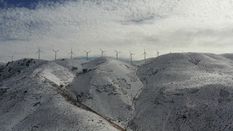 turbinas de viento giran sobre montañas cubiertas de nieve con nubes, antena