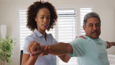 Mixed-race-female-physiotherapist-helping-senior-man-stretching-his-arms