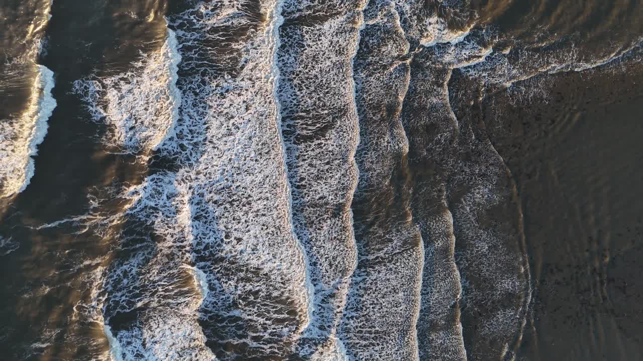 Birds eye view drone aerial view of north sea ocean waves crashing onto shore beach early morning sunrise seaburn beach sunderland england uk