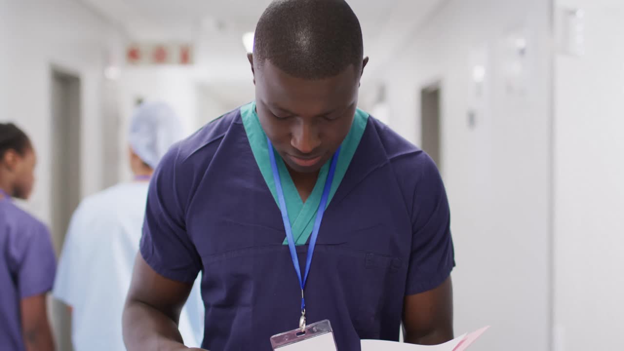 retrato de video de un trabajador médico afroamericano haciendo notas, sonriendo en el pasillo del hospital