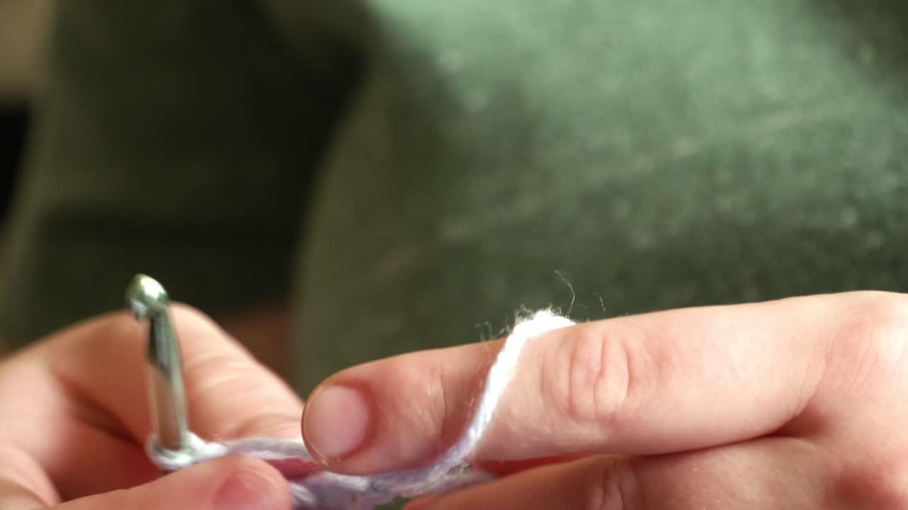 A close-up shot of caucasian hands crocheting purple yarn.