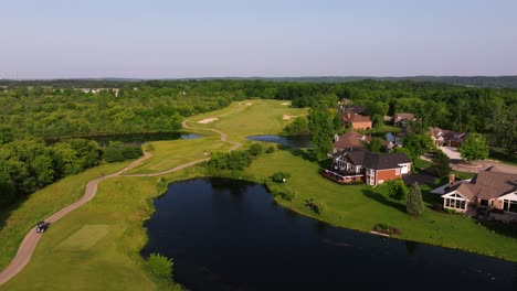 Golf course water hazard curving around bright green fairways with striped grass, aerial dolly