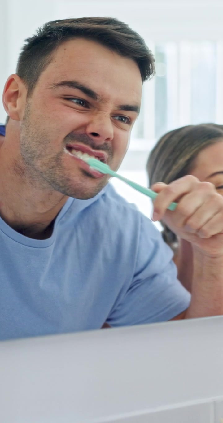Young Couple Brushing Teeth Together in Bathroom Mirror
