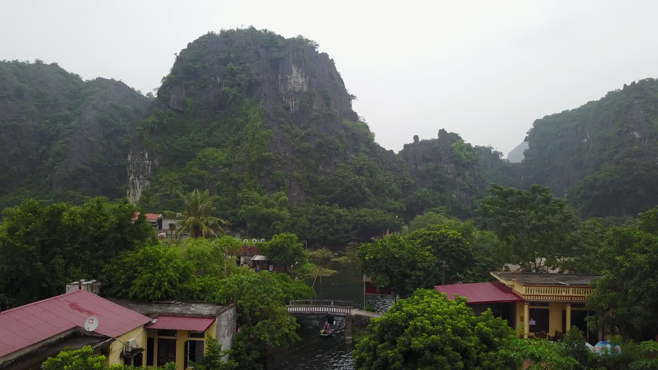 Discover the charm of small residences nestled near the towering rock formations of Ninh Binh, Vietnam. This view captures the unique way of life where homes blend with the stunning natural landscape