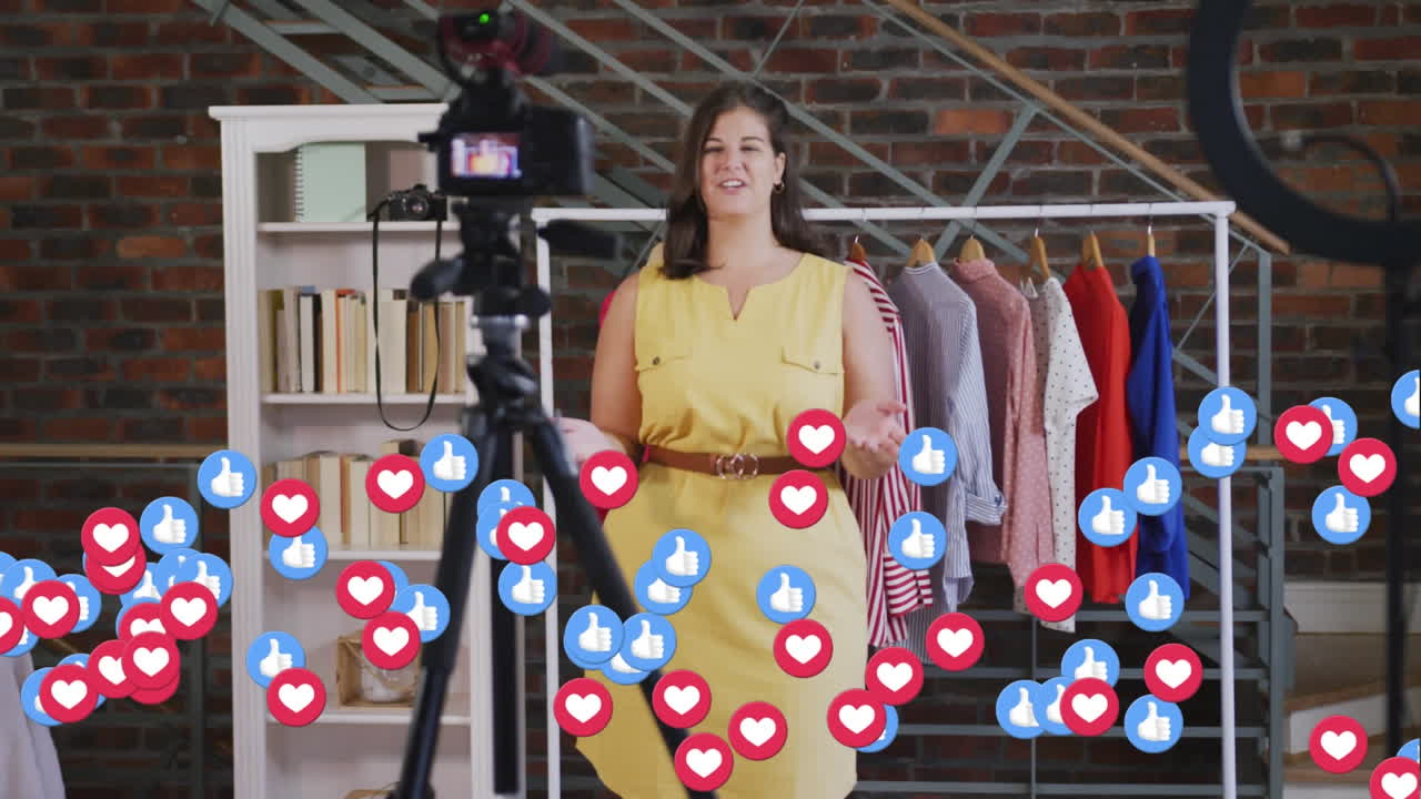 Animation of love and like icons over female fashion vlogger recording vlog at home