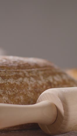 Vertical-Video-Shot-Of-Freshly-Baked-Loaves-Of-Bread-On-Work-Surface-With-Rolling-Pin