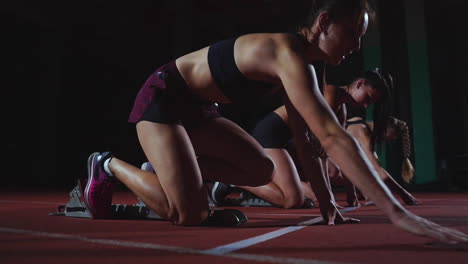 female runners at athletics track crouching at the starting blocks before a race. in slow motion.