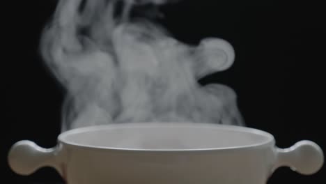 the hot tea in the white cup has white smoke and steam effect on the black background.