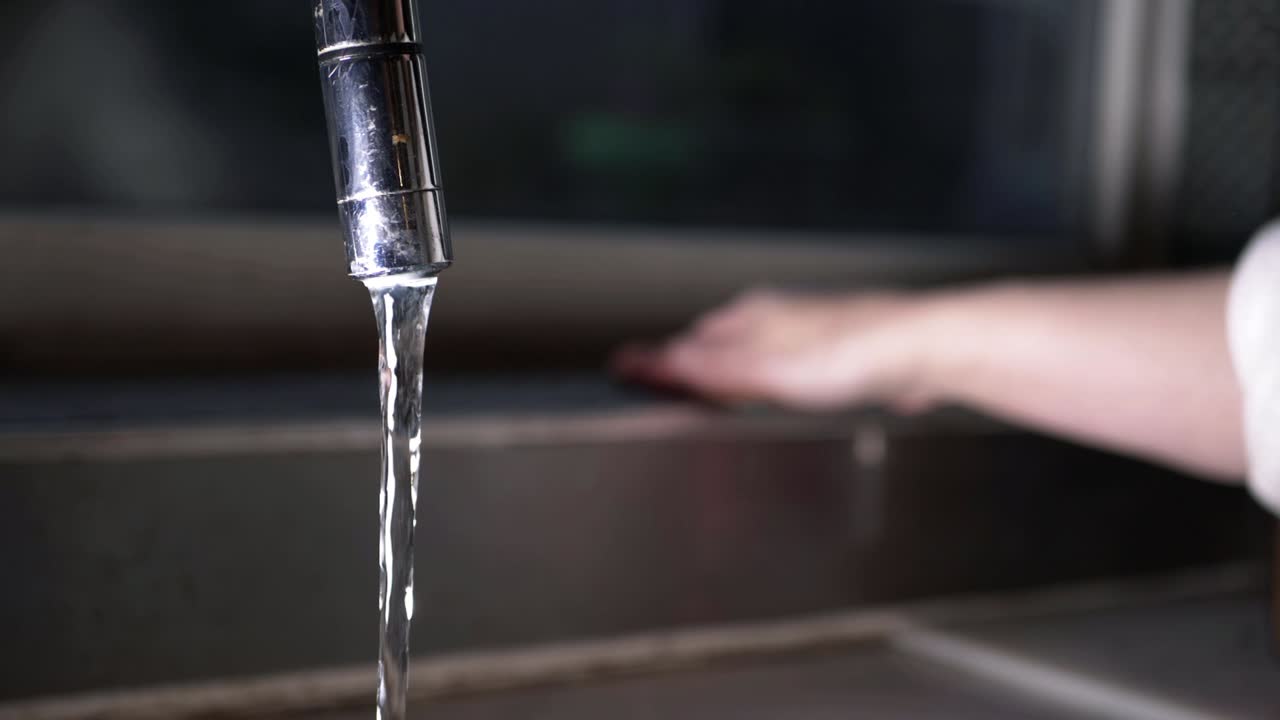 agua corriente del grifo de la cocina con una mujer limpiando al fondo