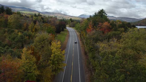 Flying-over-asphalt-road-with-cars-driving-through-colorful-autumn-forest