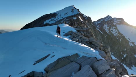 Aerial-drone-shot-pushing-out-on-a-female-mountaineer-hiking-across-a-beautiful-snowfield-at-sunrise-in-the-mountains-of-South-Tyrol,-Italy