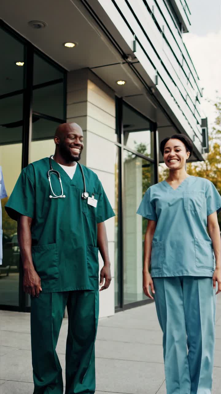 Video of two healthcare professionals in scrubs, smiling outside a modern building