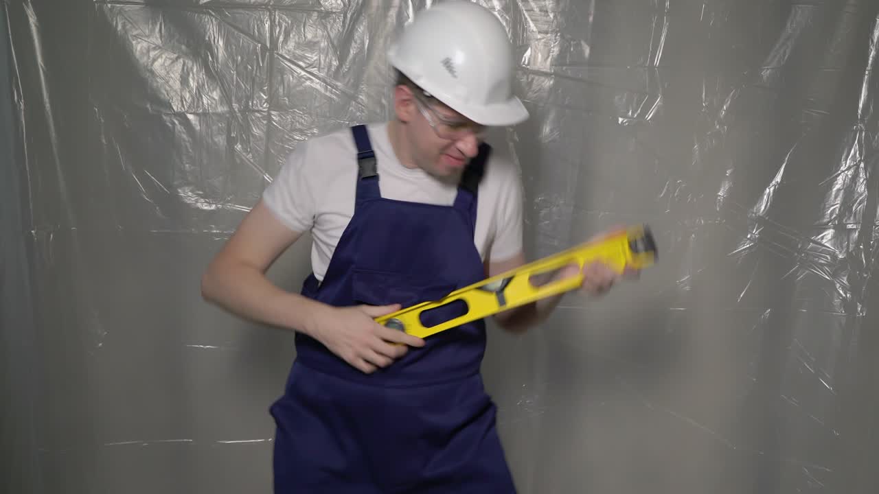 Builder in blue overalls and white hard hat. Funny playing like guitar, dancing