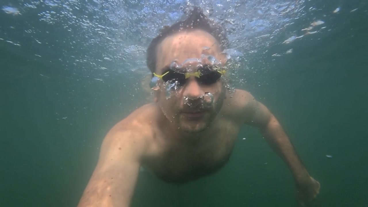 Uomo con occhialini da nuoto che esplora sott'acqua, esalando bolle d'aria. Concetto di ricreazione, sport e tempo libero.