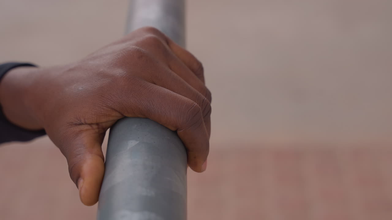 Mano che afferra una ringhiera metallica con gesso, primo piano del palmo e delle dita ruvide di un atleta che stringono una ringhiera esterna sopra una piazza in mattoni, enfatizzando forza, determinazione, tecnica di presa e resistenza
