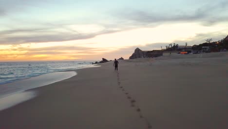 young male running along a sandy beach in cabo san lucas, mexico, at sunset