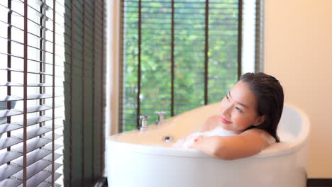 Hübsche-Asiatische-Frau-In-Der-Badewanne-Mit-Natürlichem-Licht-Aus-Den-Fenstern,-Die-Die-Aussicht-Genießen