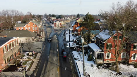 aerial pair of horse drawn-carriages moving through town during snowfall