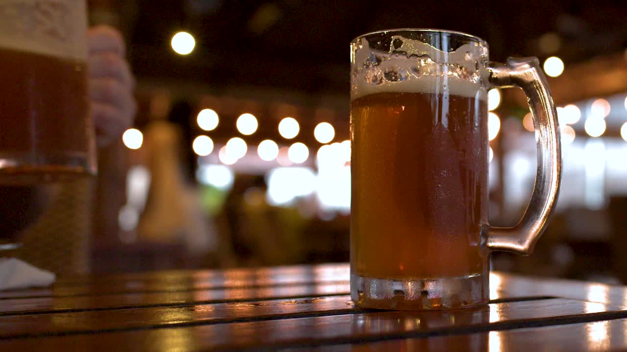 Primo piano di boccali di birra fredda con condensa su un tavolo di legno in un bar in penombra.