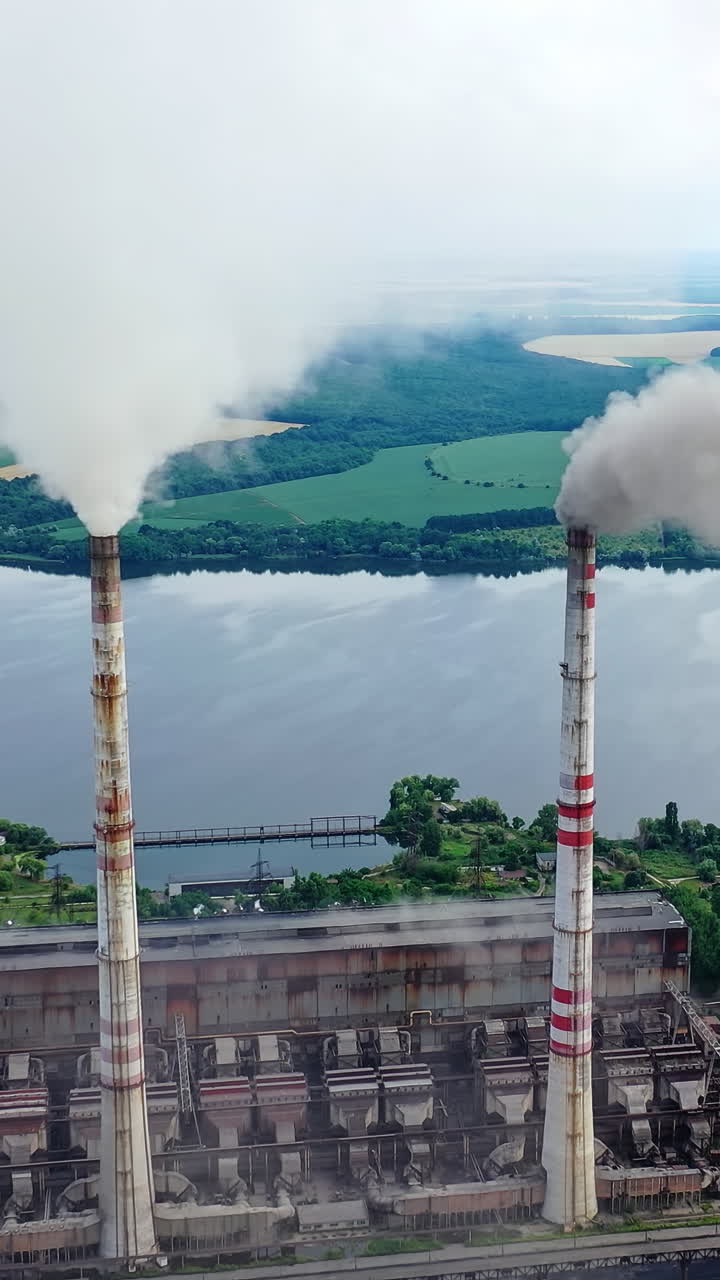 Drone shot of industrial zone with thick smog and burning fossil fuels. Factory zone pan shot left to right of polluted city, many factory chimneys in city area. Vertical video