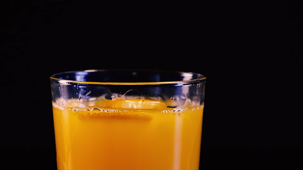 Un liquido arancione vivido schizza all'interno di un bicchiere su uno sfondo nero intenso.