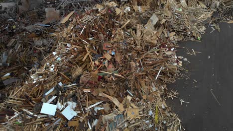 aerial top down rotating at low altitude closely over huge dumpsite filled with pile of wooden and bulky waste made up of light and dark euro pallets