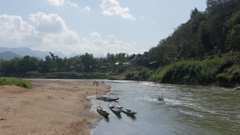 the beautiful pristine waters of the mekong river in luang prabang, laos with small boats docked by the riverbank - wide shot