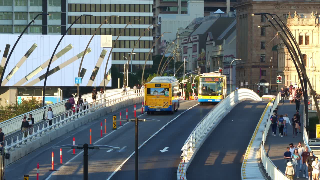 Brisbane's street scene, buses driving on Victoria bridge, pedestrians and cyclists on the walkway, set against modern and historic buildings, time-lapse shot captured from Cultural Centre station.