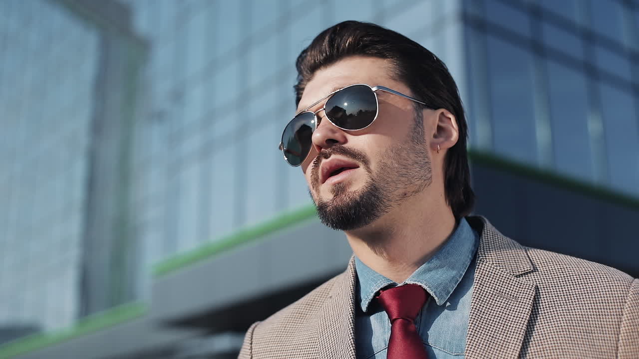 Uomo Elegante con Occhiali da Sole che Fuma una Sigaretta in Contesto Urbano
