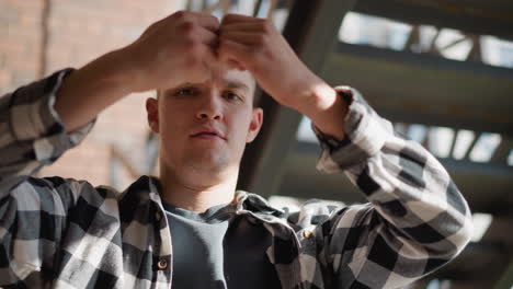man in black white plaid shirt on outdoor metal staircase clenches cigarette between fingers forces it to break in half signifying break from smoking addiction under sunlit brick wall