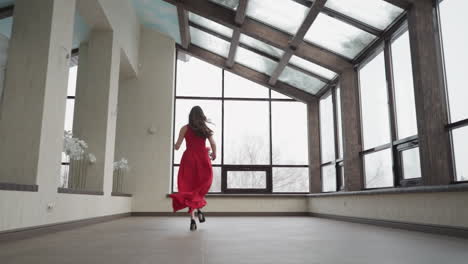 woman in long red dress runs up to window. young lady in art gallery orchestrates visually stunning episode in motion. combination of elegance and glamour