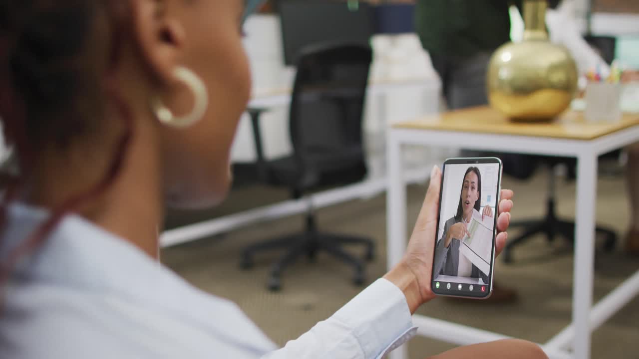 mujer de negocios afroamericana que usa un teléfono inteligente para una videollamada con un colega de negocios biracial