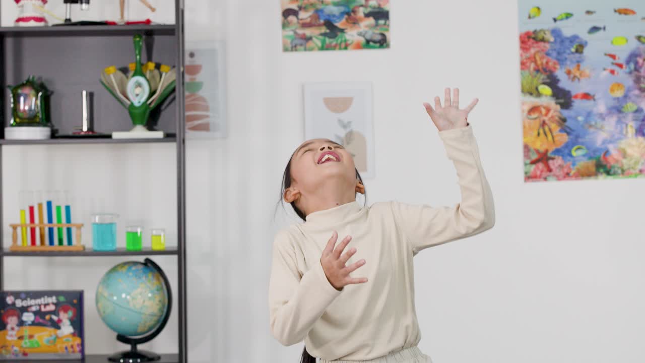 A cheerful Asian girl puts on a white lab coat and laughs in a classroom