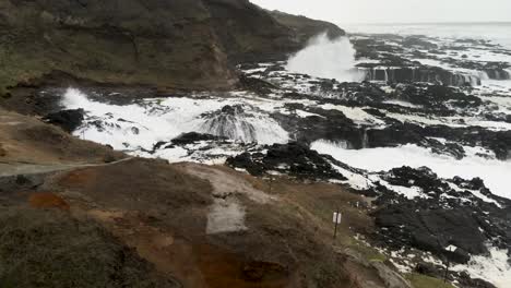 Slowly-tracking-forward-as-twin-waves-crash-upon-a-jagged-rocky-shore,-aerial