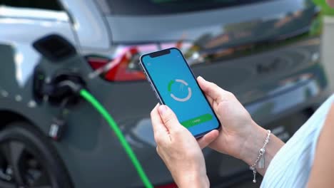 woman using a smartphone app to monitor her electric car's charging progress