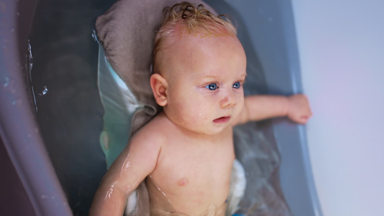 Relaxed Caucasian infant lies in the water. Lovely cute baby boy having a bath. Close up.