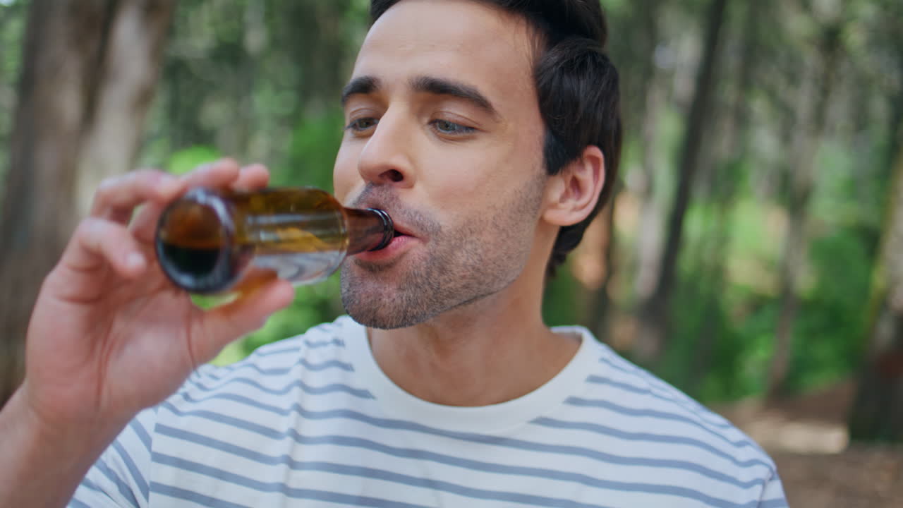 Youngsters toasting beer bottles in green park closeup. Portrait of smiling man