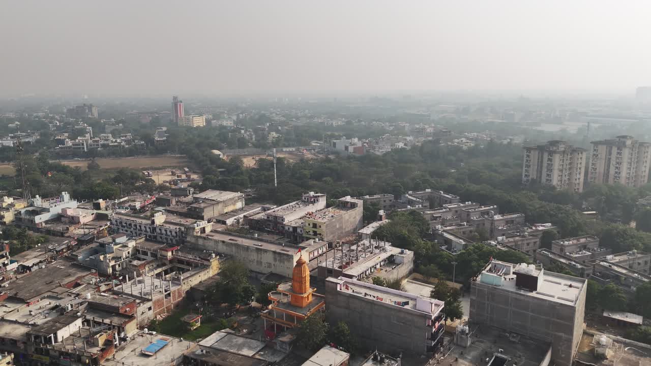 Filmato aereo su Greater Noida, che mette in evidenza i quartieri in espansione, il verde disseminato e lo sviluppo in corso, attenuato dallo smog urbano leggero all'orizzonte