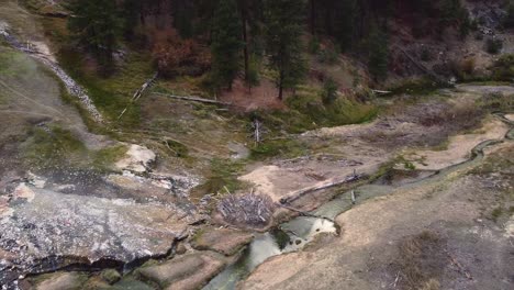 aerial drone view flying over natural sulfur hot springs in boise national forest idaho located next to a hillside and sulfurous green creek