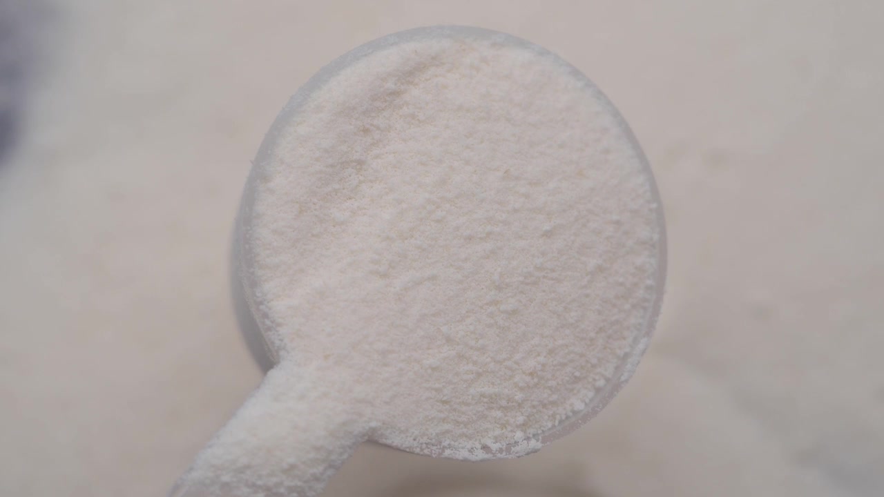 Misurino di integratore di proteine in polvere bianco.