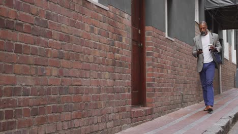 hombre afroamericano caminando por la calle y usando su teléfono