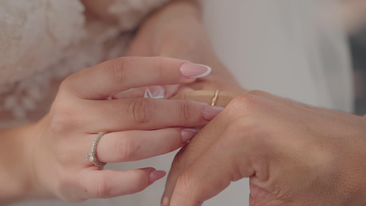 Close up of bride’s hand putting gold wedding ring on groom’s finger during ceremony