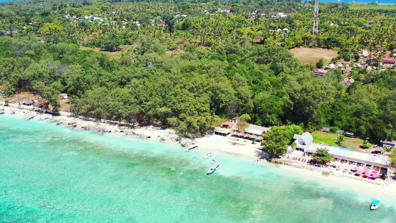 Peaceful exotic beach with bar restaurants near white sand washed by calm turquoise lagoon on tropical island with green trees forest, Bali