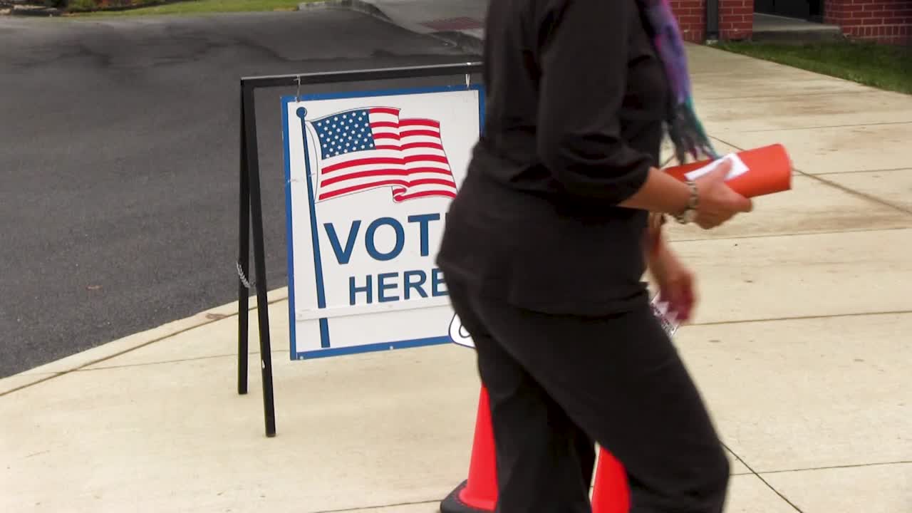 People walk by vote here sign with American flag and wheelchair handicapped friendly signs