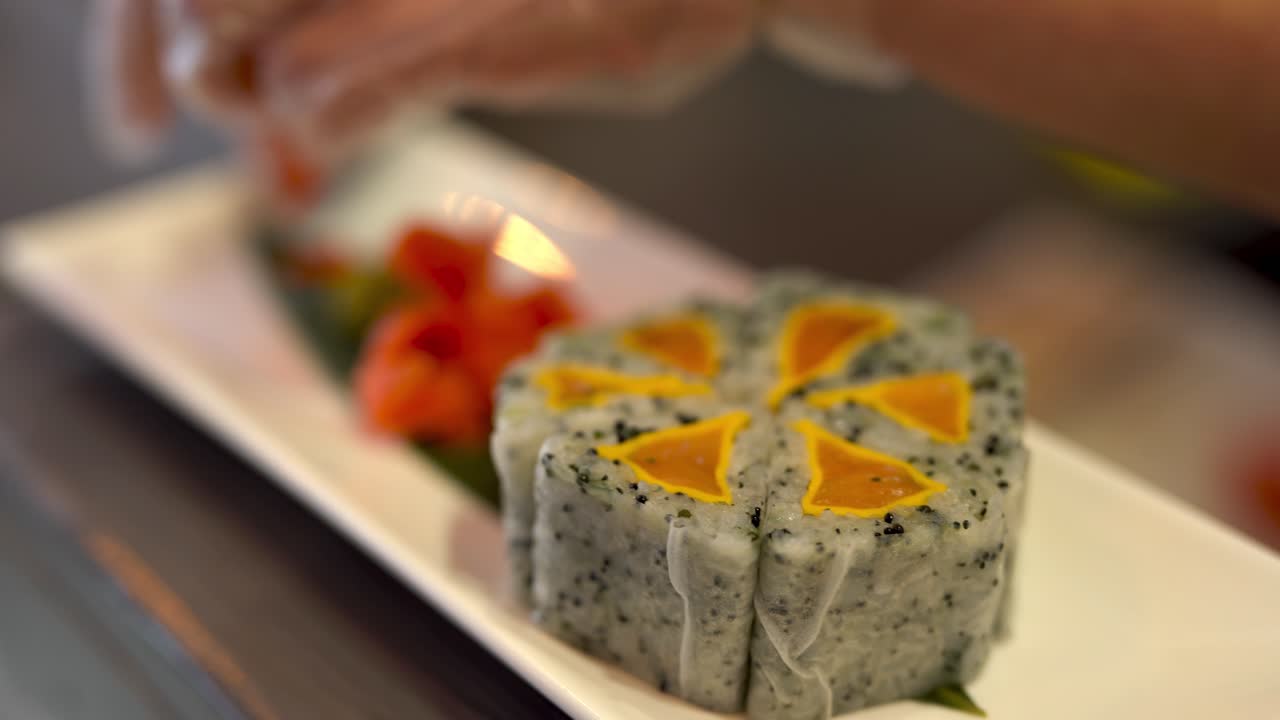 o rolo de sushi uramaki está pronto a ser servido, mas o cozinheiro coloca os últimos pedaços para decoração, nomeadamente caviar vermelho, no prato e na folha de bambu