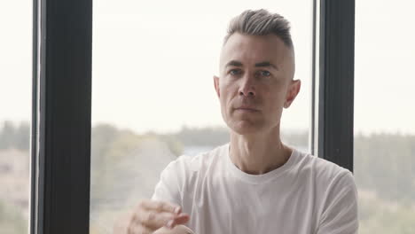 portrait of a pensive man sitting by the window and looking at camera